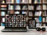 ein PC, ein Tablet, eine Powerbank und Kopfhörer sind vor einem Bücherregal zu sehen
